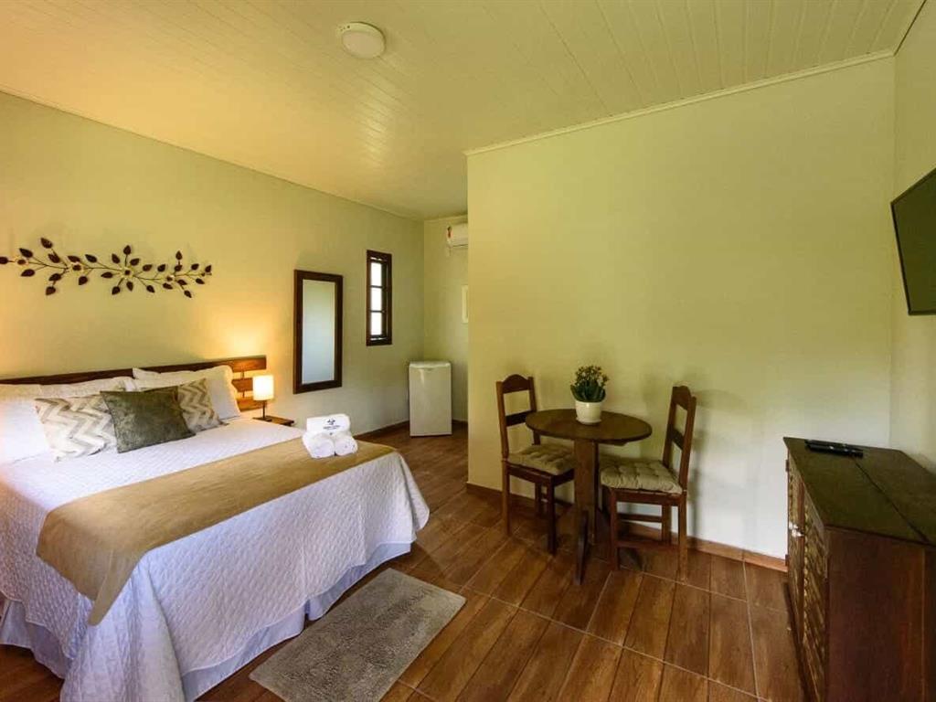Quarto com cama, televisão e banco de madeira