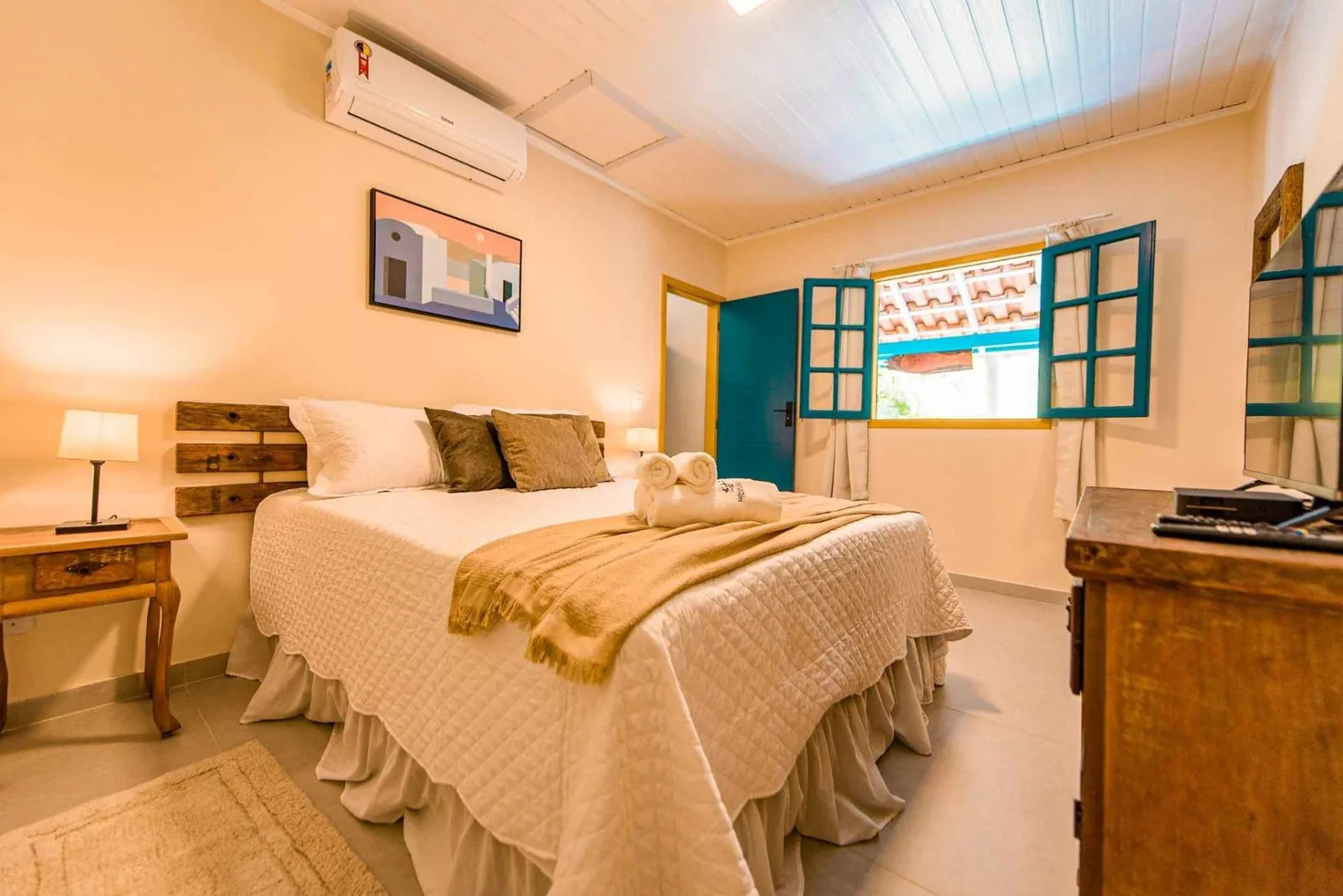 Quarto com cama de casal, janelas de madeira e poltrona