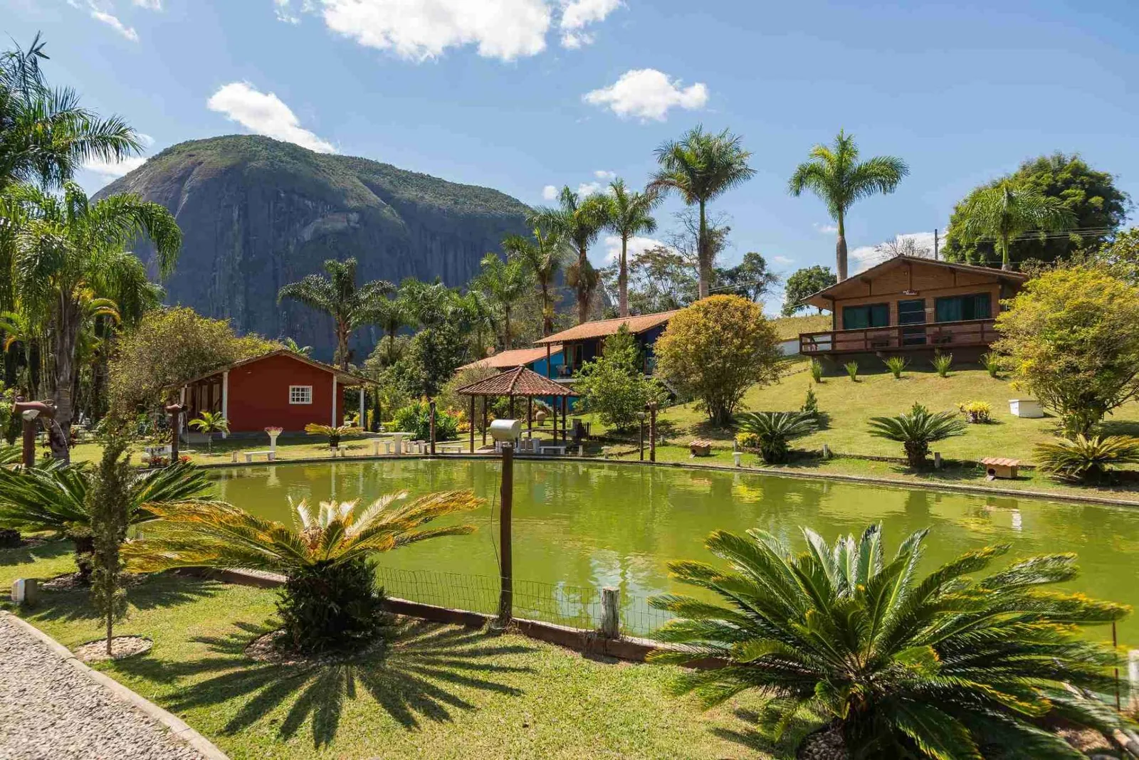 Lago rodeado por palmeiras, jardins e chalés, com montanha ao fundo