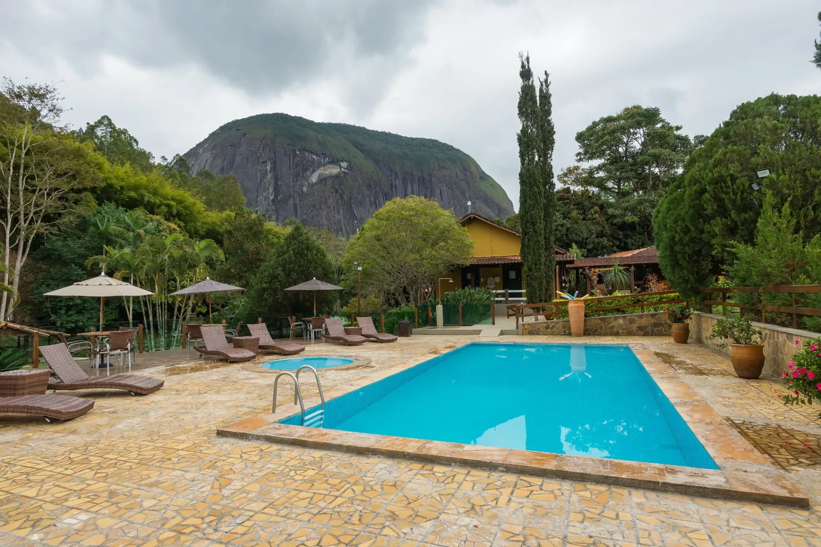 Piscina com deck de pedra, espreguiçadeiras e montanha ao fundo