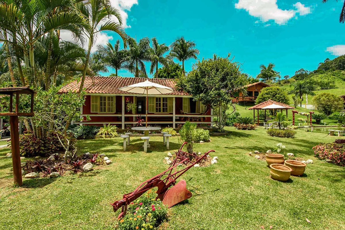 Casa de fazenda com varanda, jardim e antigo arado no gramado